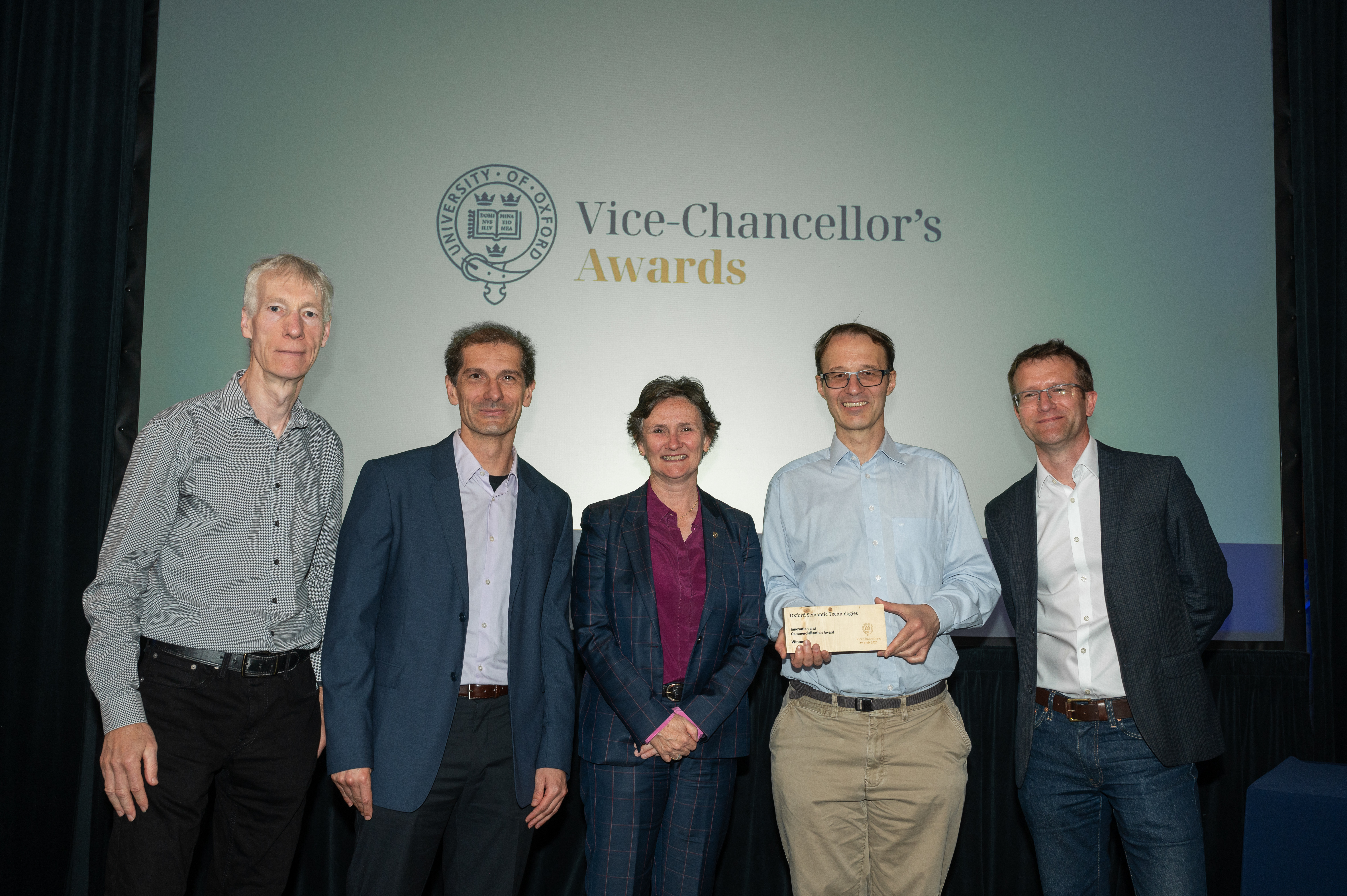 A photograph of five people standing in front of a screen that reads 'Vice-Chancellor's Awards'. All five people are looking towards the camera and smiling, they are all wearing smart shirts and trousers.
