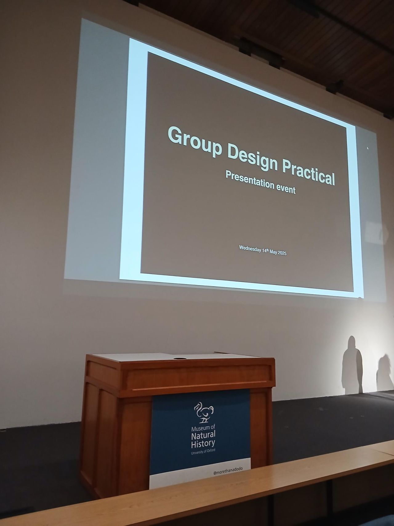 A podium says 'Oxford University Museum of Natural History' and behind a projected screen says 'Group Design Practical'
