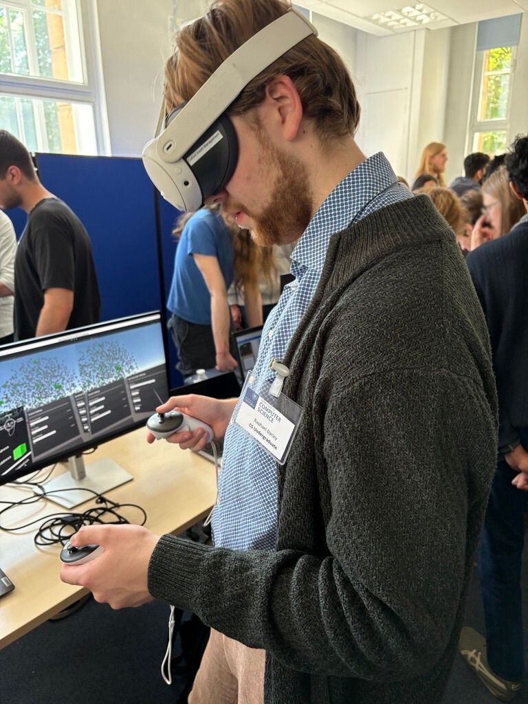 A student wears a VR headset and is looking down in concentration. They are surrounded by many other people milling around looking at screens and talking to researchers.